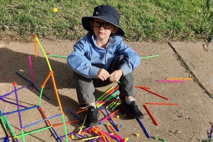 A student is creating a STEM tower on the path outside the classroom